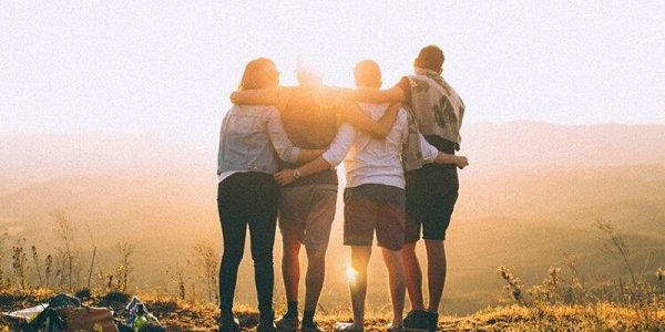 Four people embracing on a sunny hilltop.
